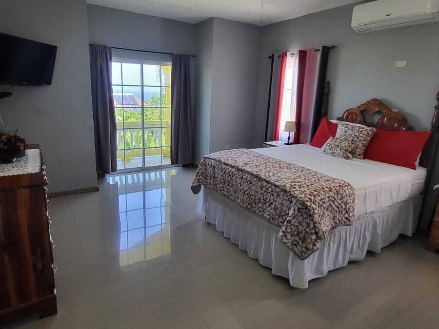 A bedroom with a bed, a dresser, a TV, and a window with curtains.