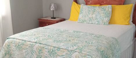 A bedroom with a bed, a nightstand, a lamp, and a wall-mounted light fixture.