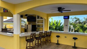 A bar area with a counter, stools, and a ceiling fan. - Kingsbird by the sea Inn  (Discovery Bay)
