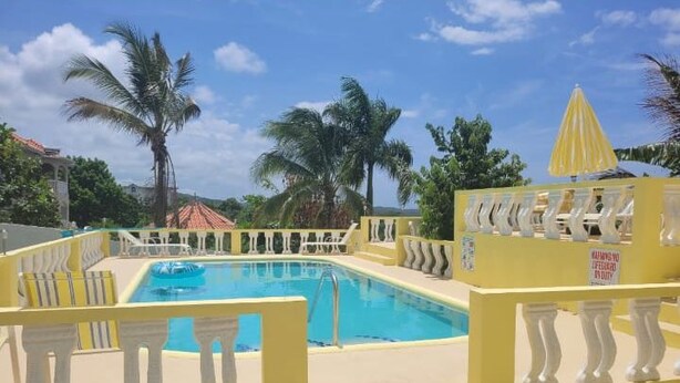 A swimming pool with yellow railings and palm trees in the background. - Kingsbird by the sea Inn  (Discovery Bay)