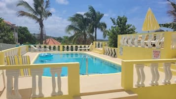 A swimming pool with yellow railings and palm trees in the background.