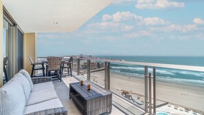 A balcony with wicker furniture, a glass railing, and a view of the beach and ocean.