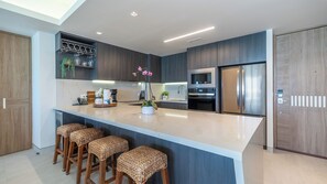 Une cuisine moderne dotée d’un îlot central, de tabourets de bar, d’appareils électroménagers intégrés et d’une porte en bois.