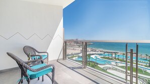 A balcony with wicker chairs and a view of a resort with pools and a beach.