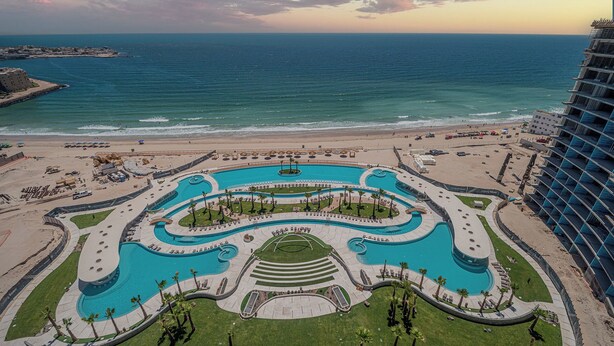 A resort with a large central pool, a beach area, and ocean views.