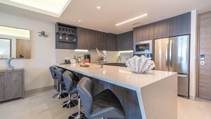A modern kitchen with a central island, bar stools, a refrigerator, and a microwave.