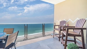 A balcony with a view of the ocean, wooden chairs, a table, and a small plant.