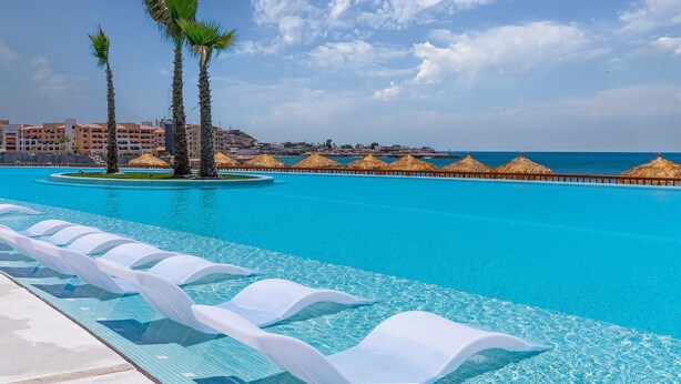 Une piscine d’un complexe hôtelier avec une eau d’un bleu cristallin, des palmiers et une vue sur l’océan.