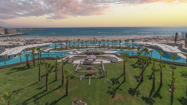 A resort with multiple swimming pools, palm trees, and a beach area.