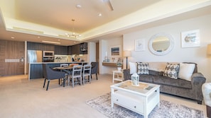 A modern living room with a grey sofa, white coffee table, and dining area with chairs and a kitchen in the background.