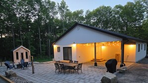A building with a covered patio, outdoor seating, and a small shed. - Sauna Retreat Near Burk's Falls | Games Room • Bocce Court • Fire Pit • Starlink (Burk's Falls)