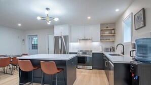 A modern kitchen with a central island, stainless steel appliances, and a water dispenser. - Sauna Retreat Near Burk's Falls | Games Room • Bocce Court • Fire Pit • Starlink (Burk's Falls)