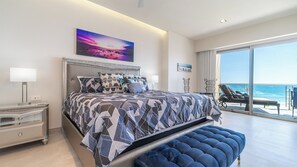 A modern bedroom with a large bed, a view of the ocean, and a balcony with outdoor seating.