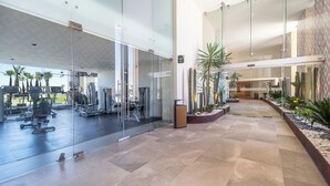 Un gimnasio con equipo de ejercicio, paredes de vidrio y un corredor con plantas.