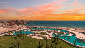 A resort with a large pool, palm trees, and a view of the ocean at sunset. - One 1204A Studio: Stylish Oceanfront Studio Retreat with Breathtaking Views (Puerto Peñasco)