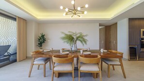 A modern dining area with a wooden table, six chairs, a central plant, and a contemporary chandelier.
