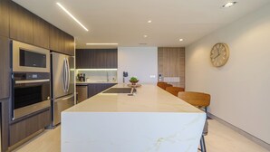 Een moderne keuken met inbouwapparatuur, een marmeren aanrechtblad en een eethoek met een klok aan de muur.