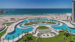 A resort with a large, winding pool surrounded by palm trees and a beach. - One 1002-Full – Modern Elegance Meets the Sea of Cortez at This Premier Destination (Puerto Peñasco)