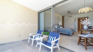 A modern room with a bed, a desk, and two chairs. There is a sliding glass door leading to another room. - One 1002: Hotel Room– Luxury Oceanfront Condo with Stunning Views (Puerto Peñasco)