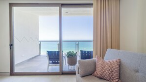 A room with a sliding glass door leading to a balcony with a view of the sea. There is a sofa with a patterned pillow and a potted plant on the balcony. - One 1002: Hotel Room– Luxury Oceanfront Condo with Stunning Views (Puerto Peñasco)