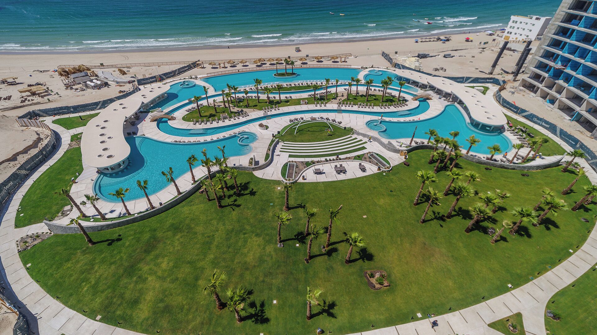 Een resort met een groot, kronkelend zwembad, omringd door palmbomen en een strand.
