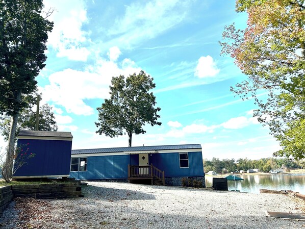 A blue cabin with a dock by a lake, surrounded by trees.