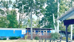 A blue cabin with a deck, surrounded by trees and a stone wall.