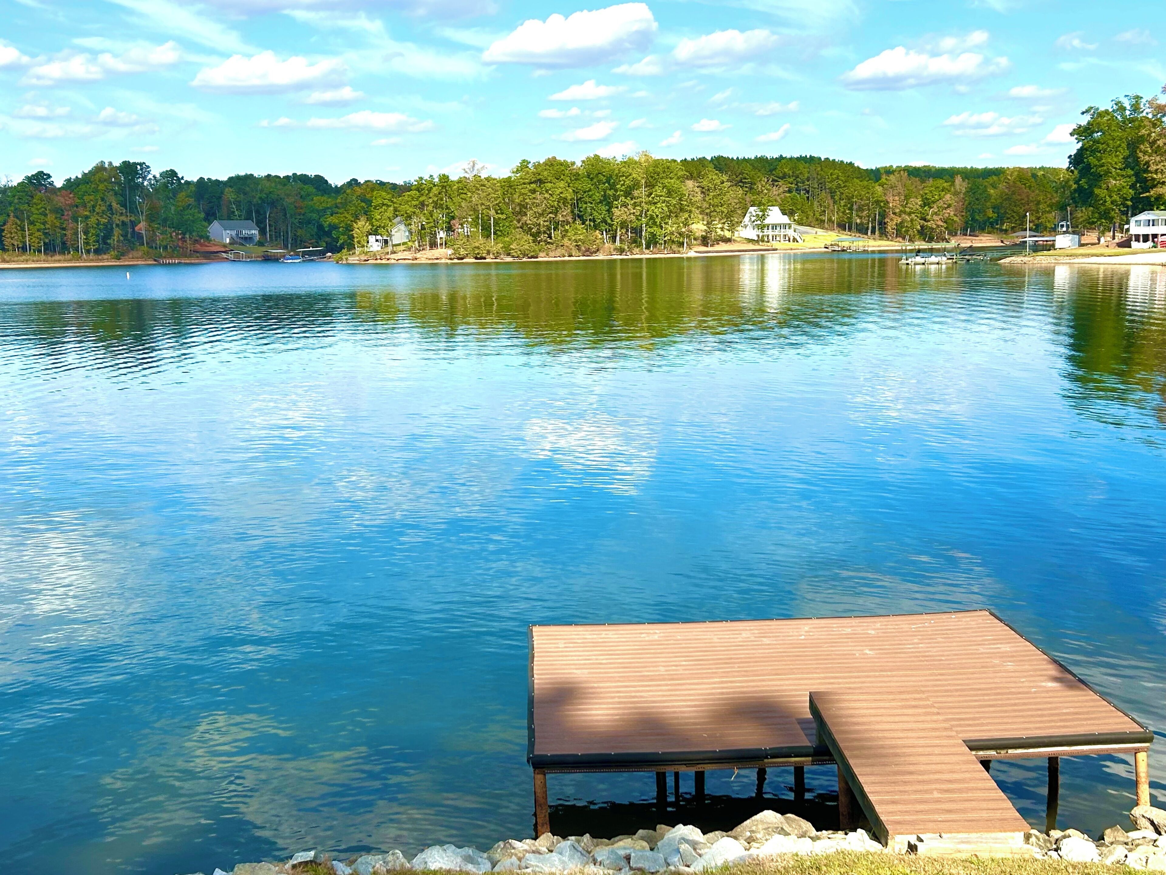 A wooden dock extending into a calm lake with a backdrop of trees and houses.