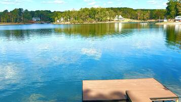 A wooden dock extending into a calm lake with a backdrop of trees and houses.