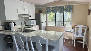 A kitchen with white cabinets, a microwave, a stove, and a sink. There are two white chairs and a table.