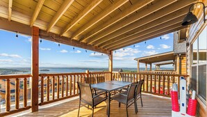 Une terrasse en bois avec une table et des chaises, d’où l’on peut admirer un plan d’eau et un paysage lointain.