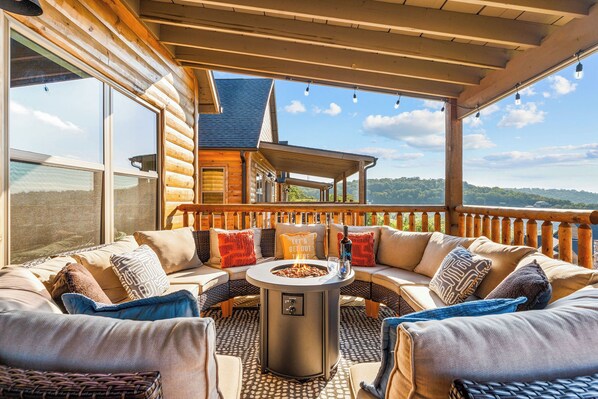 A cozy outdoor seating area with a fire pit, wooden furniture, and a view of a mountain landscape.