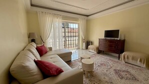 Uma sala de estar com sofá, televisão, cômoda e tapete estampado.