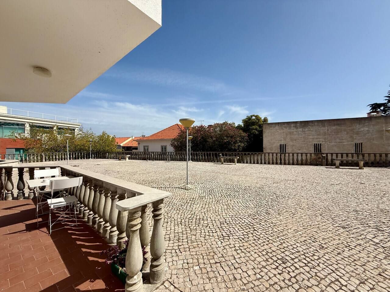 Ein Innenhof mit Kopfsteinpflasterboden, einem weißen Tisch mit Stühlen und einem Laternenpfahl.