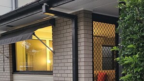 Een gebouw met een bakstenen gevel, een raam met een geel luifel en een zwart metalen hek.