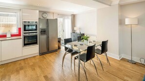 Une cuisine moderne dotée d’appareils électroménagers en acier inoxydable, un coin repas avec une table en verre et des chaises noires, et un plancher en bois.