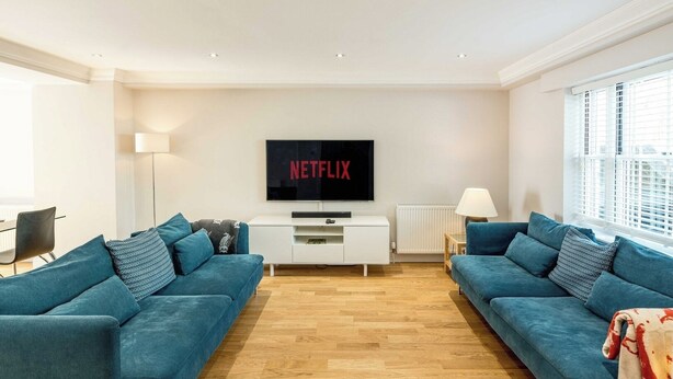 Un salon moderne avec deux canapés bleus, un meuble de rangement blanc et un grand téléviseur à écran plat affichant le logo « NETFLIX ».