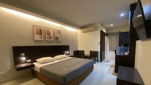 A modern hotel room with a bed, bedside table, wall-mounted artwork, a desk, and a TV. - Suansin Lanna Hotel (Tak)