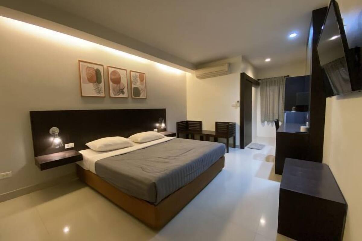 A modern hotel room with a bed, bedside table, wall-mounted artwork, a desk, and a TV.