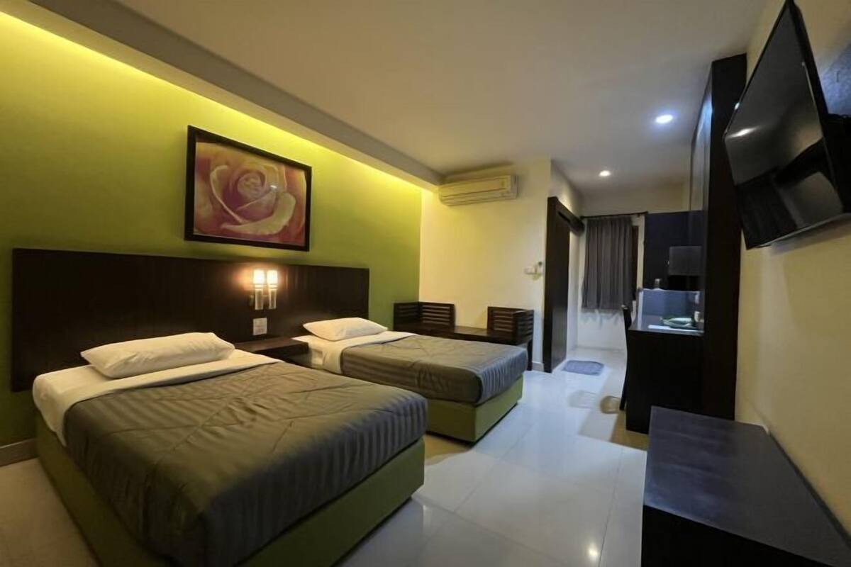 A hotel room with two beds, a TV, a painting, and a desk with a lamp.