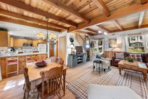 Uma sala de estar espaçosa com teto de madeira, mesa de jantar com cadeiras, sofá e mesa de centro.