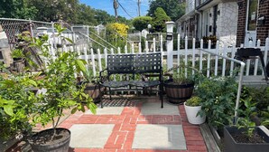 Un patio con pavimento in mattoni, una panchina in metallo nero e piante in vaso.