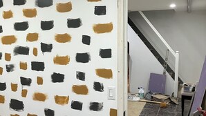 Una stanza in ristrutturazione con un muro decorato, una porta ben visibile e una scala sullo sfondo.