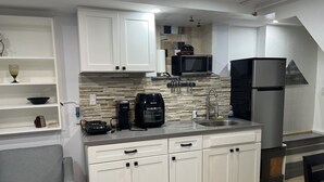 Una cucina moderna con mobili bianchi, forno a microonde integrato, macchina da caffè e frigorifero.