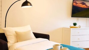 A neatly made bed with a blue throw blanket, a bedside table with a tray holding two cups, a black floor lamp, and a TV on the wall. - Sleeps 5  Peaceful  King Bd  Walk Score 98 (Philadelphia)