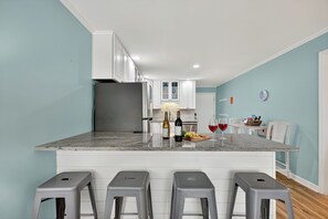 A kitchen with white cabinets, a granite countertop, and a refrigerator. There are three bar stools in front of the counter.