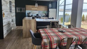 A modern kitchen with a central island, large windows, and a view of the outdoors. - L'étoile du lac Lyster (Coaticook)