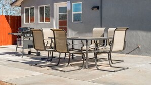 Une terrasse extérieure avec une table et des chaises, un barbecue, et une maison en arrière-plan.