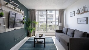 A modern living room with a flat-screen TV, a grey sofa, a coffee table, and a large window with curtains.