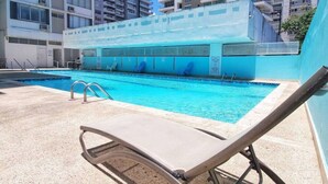 A swimming pool with a clear blue water, surrounded by a concrete deck and a few lounge chairs.